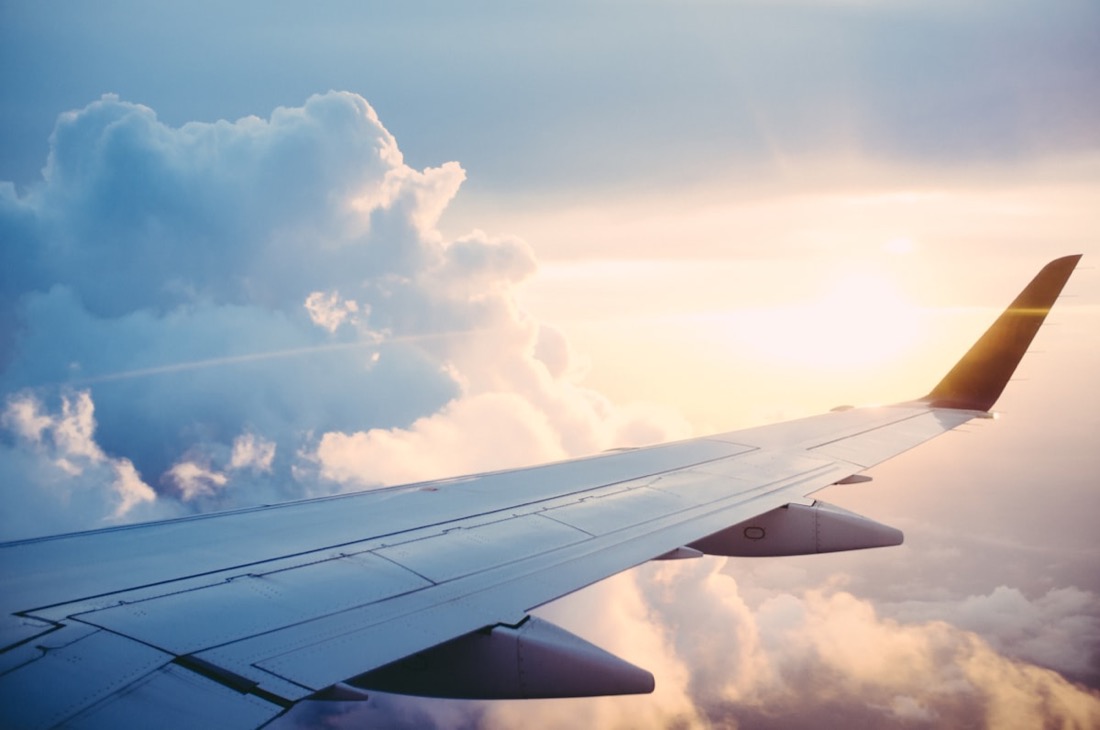 An aircraft wing above a sea of clouds at golden hour